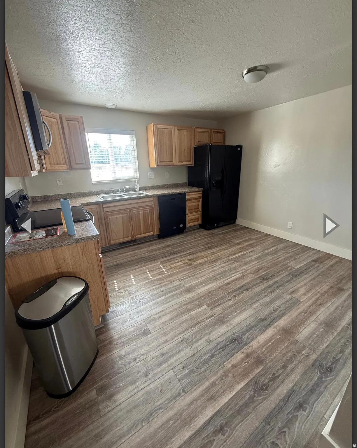 Kitchen featuring a textured ceiling, black appliances, dark wood-type flooring, and dark countertops