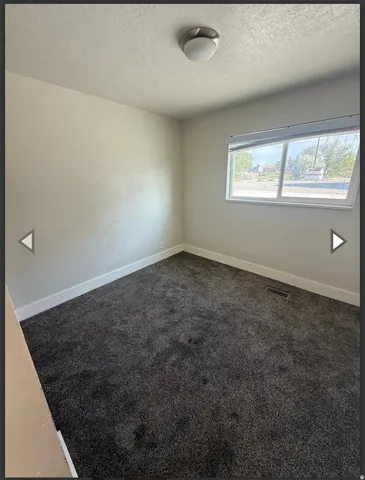 Empty room featuring dark carpet and a textured ceiling