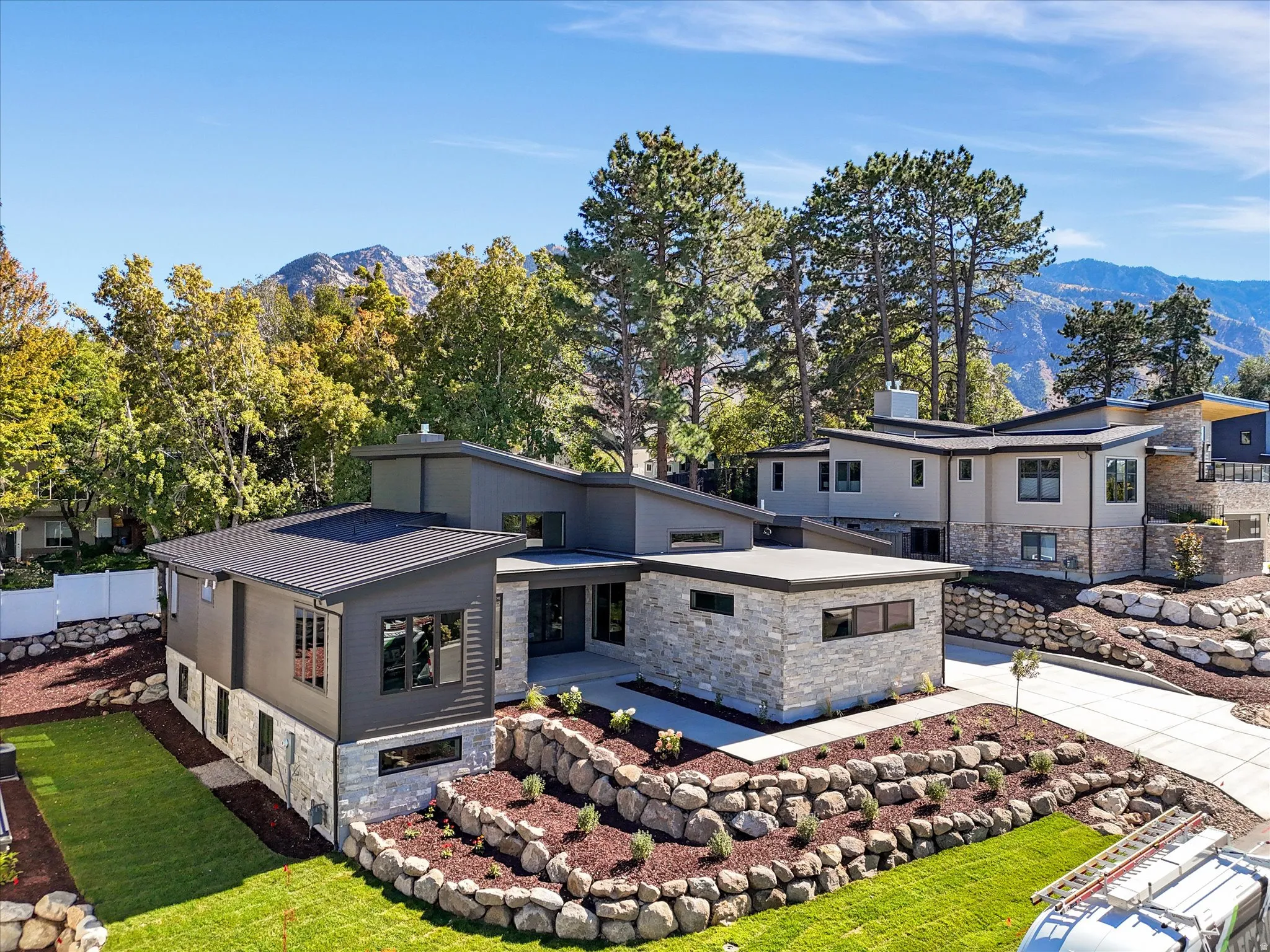 Modern home with stone siding, a mountain view, a metal roof, and a patio