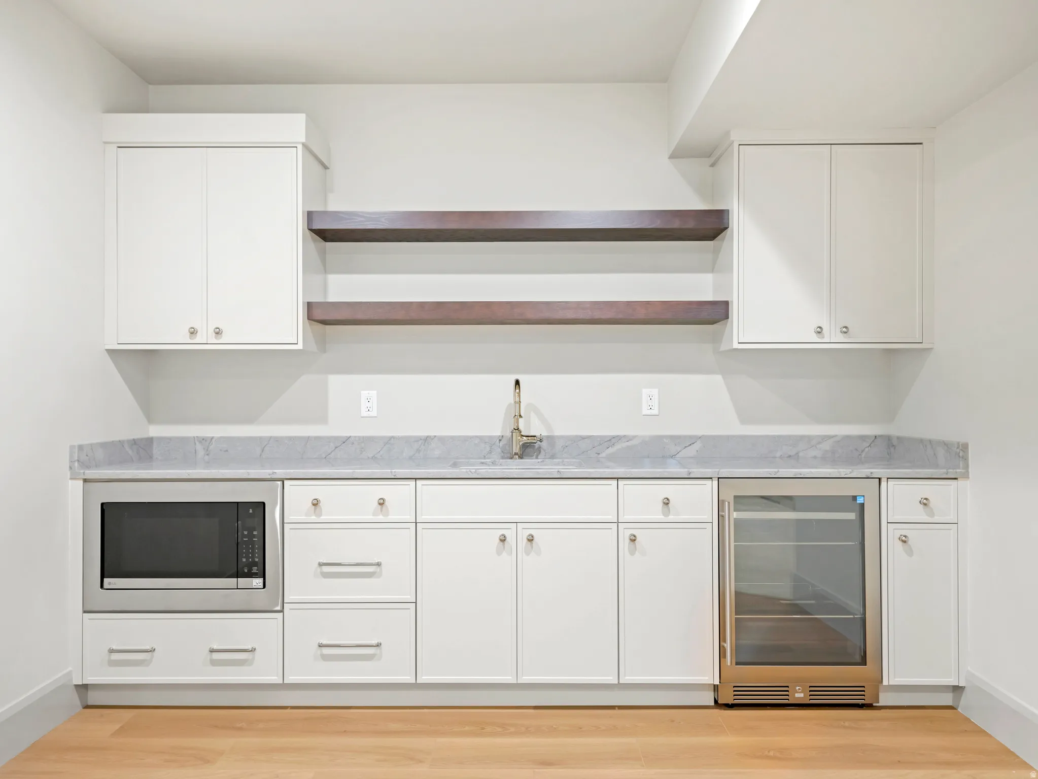 Kitchen with open shelves, wine cooler, white cabinetry, light wood-type flooring, and stainless steel microwave