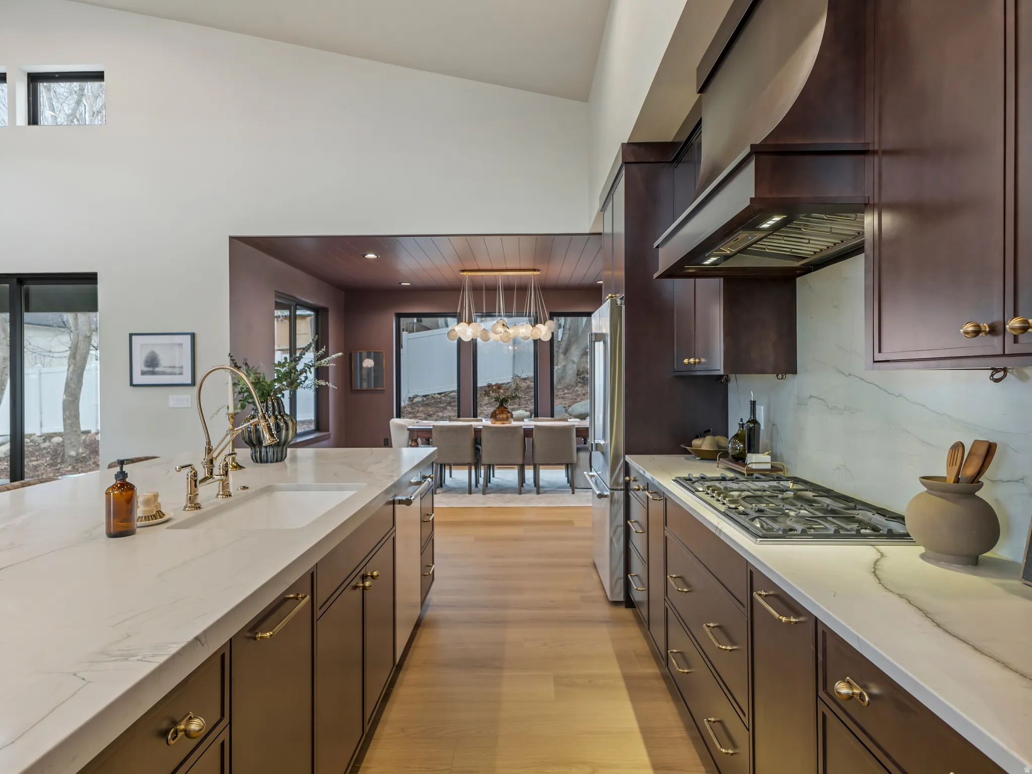 Kitchen featuring dark wood finish cabinets, light wood finished floors, light stone countertops, stainless steel appliances, and decorative light fixtures