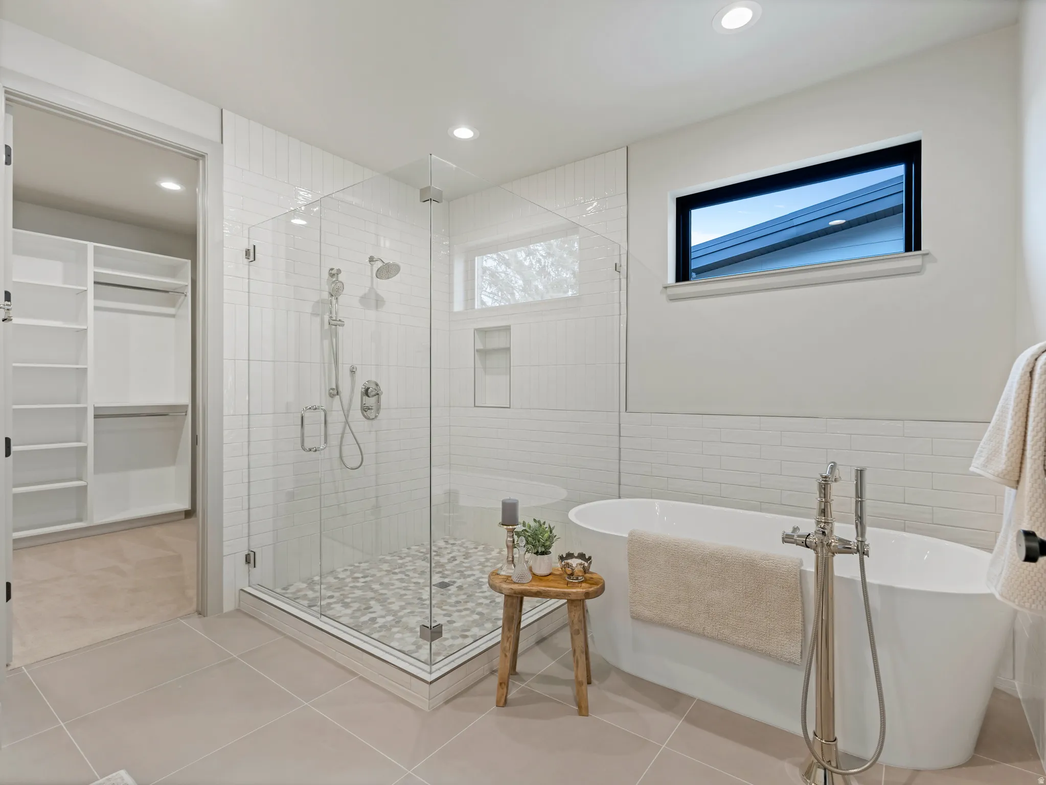 Bathroom with a freestanding tub, a stall shower, a spacious closet, light tile patterned flooring, and tile walls