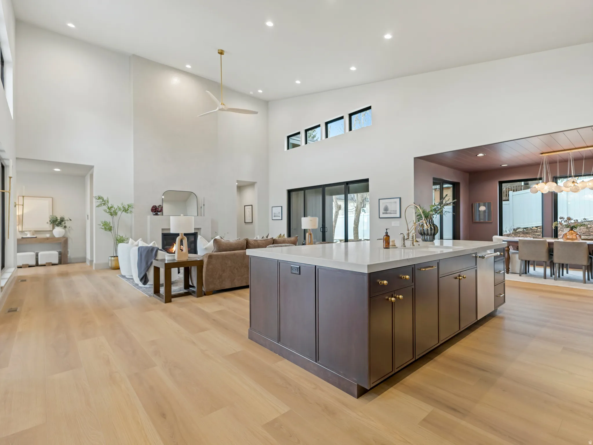 Kitchen with open floor plan, an island with sink, dark wood finish cabinetry, light wood finished floors, and a high ceiling