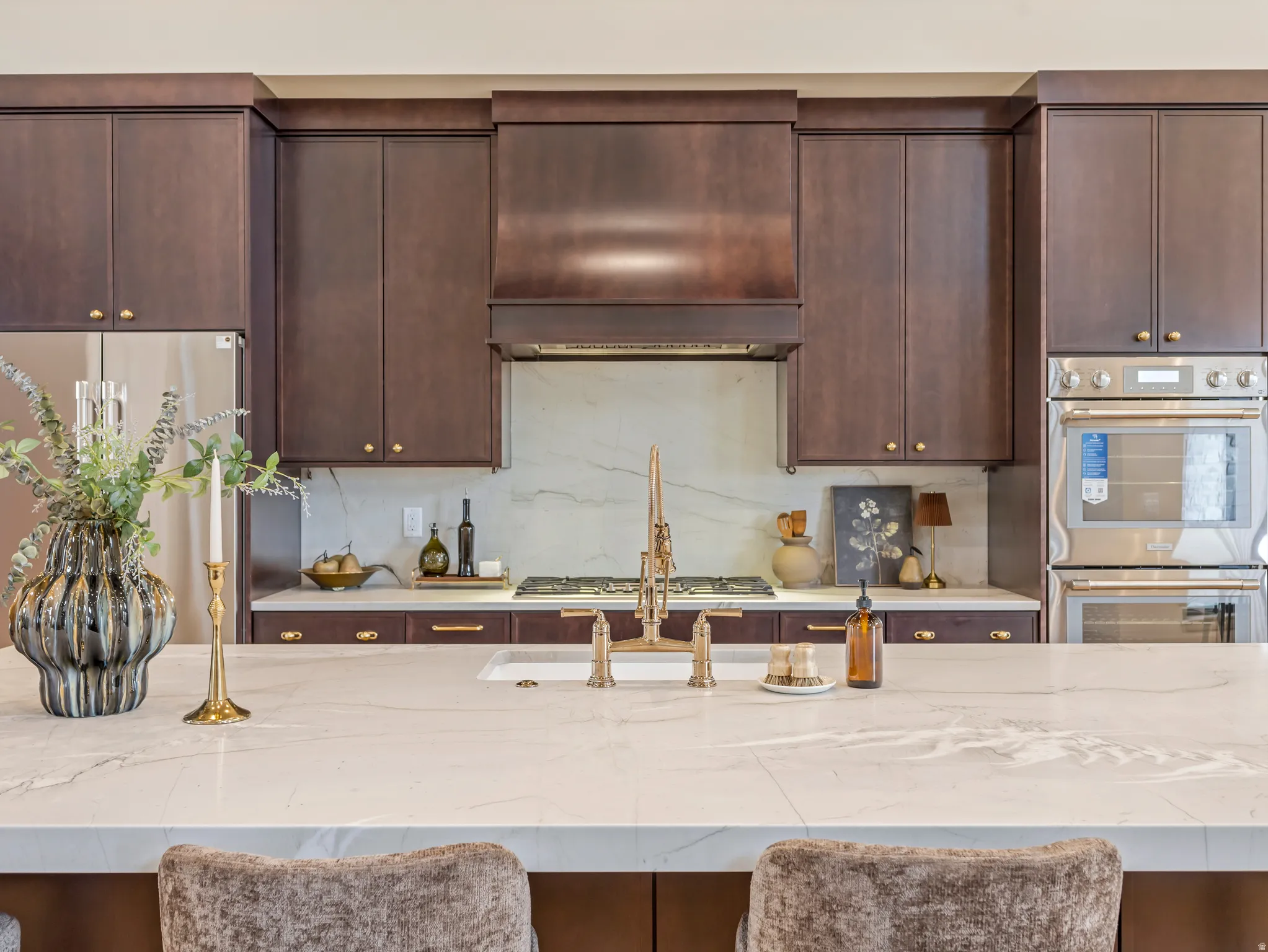 Kitchen featuring dark wood finish cabinets, stainless steel appliances, light stone counters, and extractor fan