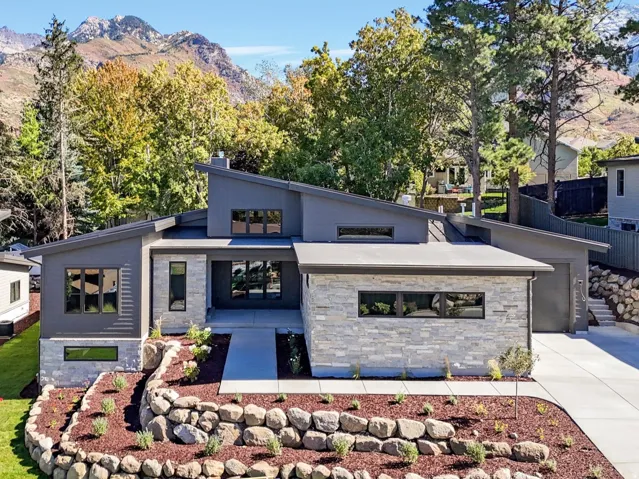 Modern home featuring stone siding, a mountain view, a front lawn, and driveway