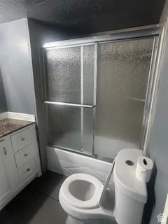 Bathroom featuring vanity, dark tile patterned floors, and bath / shower combo with glass door