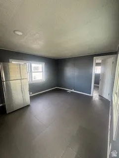 Unfurnished bedroom featuring freestanding refrigerator, multiple windows, and a textured ceiling