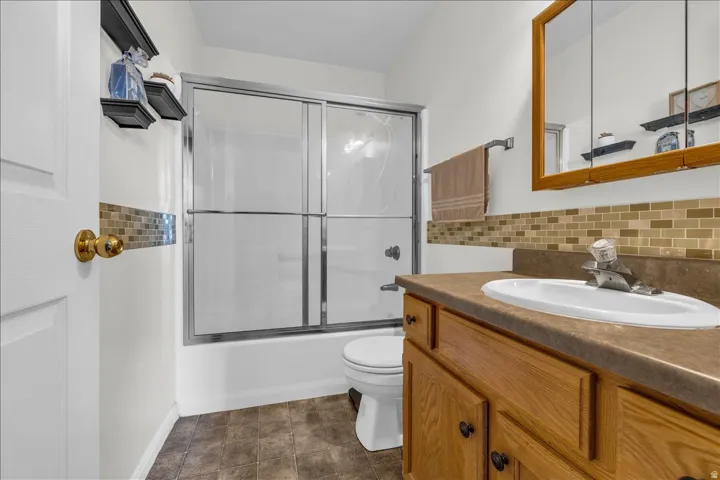 Bathroom with vanity, shower / bath combination with glass door, and decorative backsplash