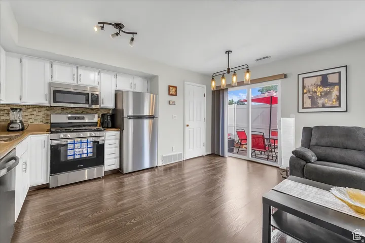 Kitchen featuring stainless steel appliances, white cabinets, dark wood finished floors, hanging light fixtures, and decorative backsplash