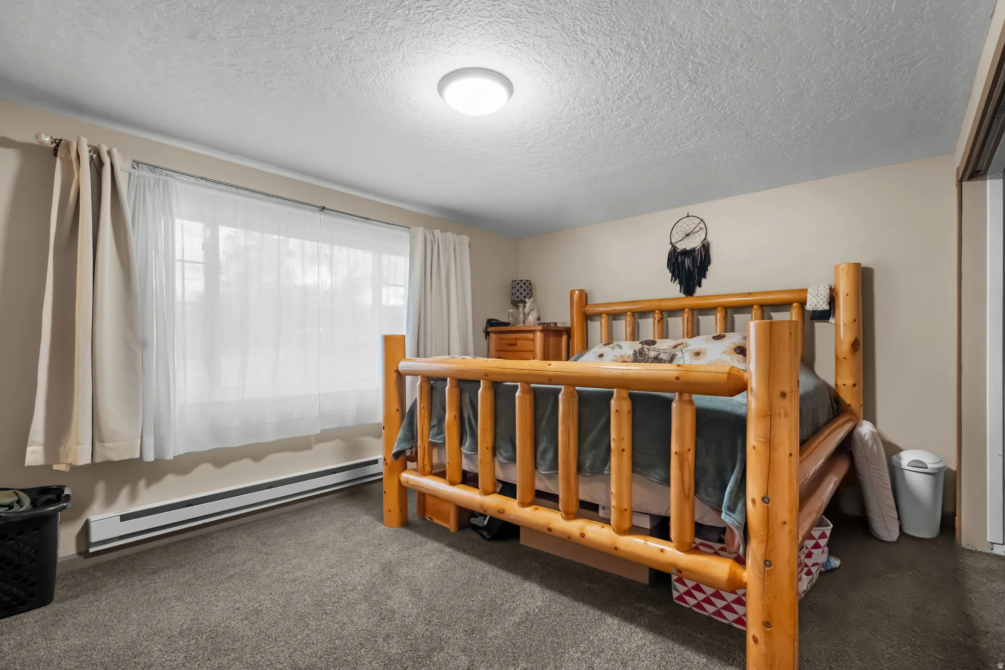 Bedroom with dark colored carpet, a textured ceiling, and baseboard heating