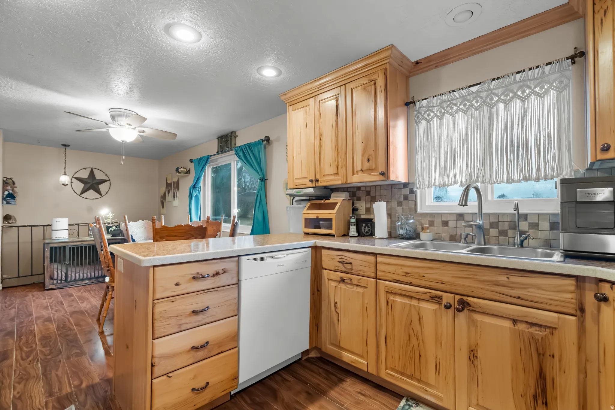 Kitchen with a peninsula, light countertops, white dishwasher, decorative backsplash, and a ceiling fan