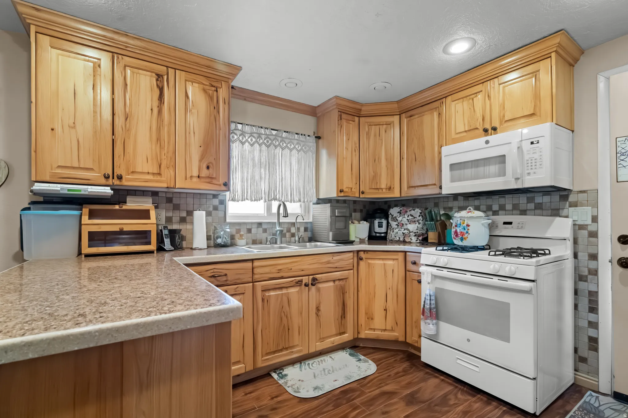 Kitchen featuring white appliances, light countertops, dark wood finished floors, decorative backsplash, and light wood finish cabinetry