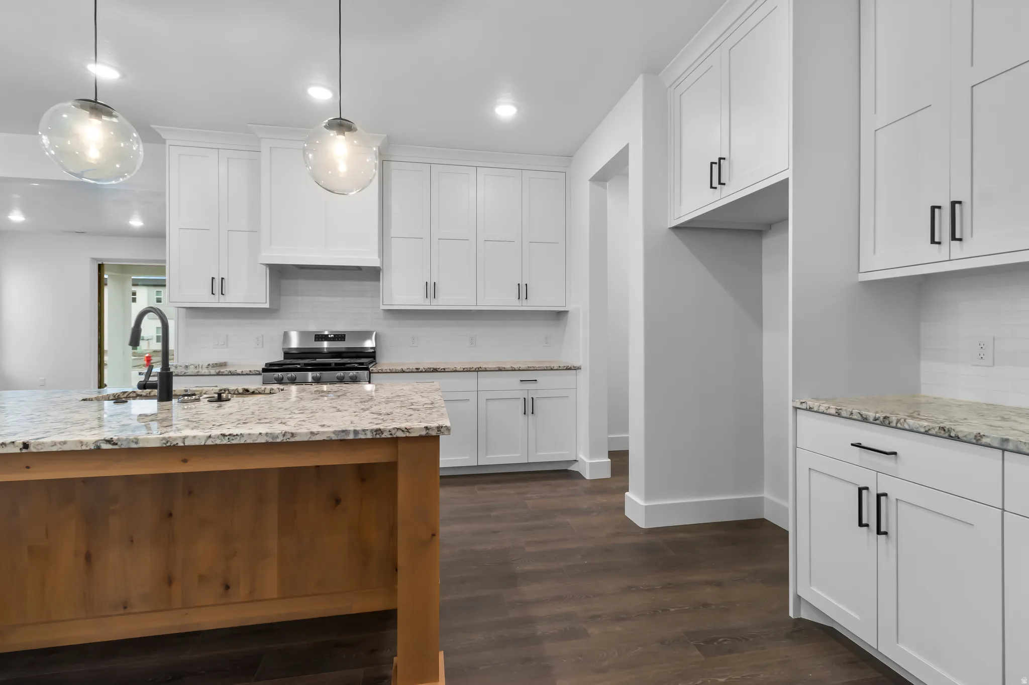 Kitchen with decorative backsplash, white cabinetry, light stone countertops, and stainless steel range oven