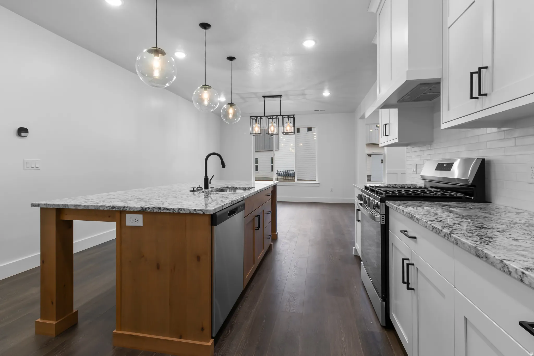 Two tone kitchen featuring stainless steel appliances, two tone color scheme, dark wood-style floors, light stone countertops, and an island with sink
