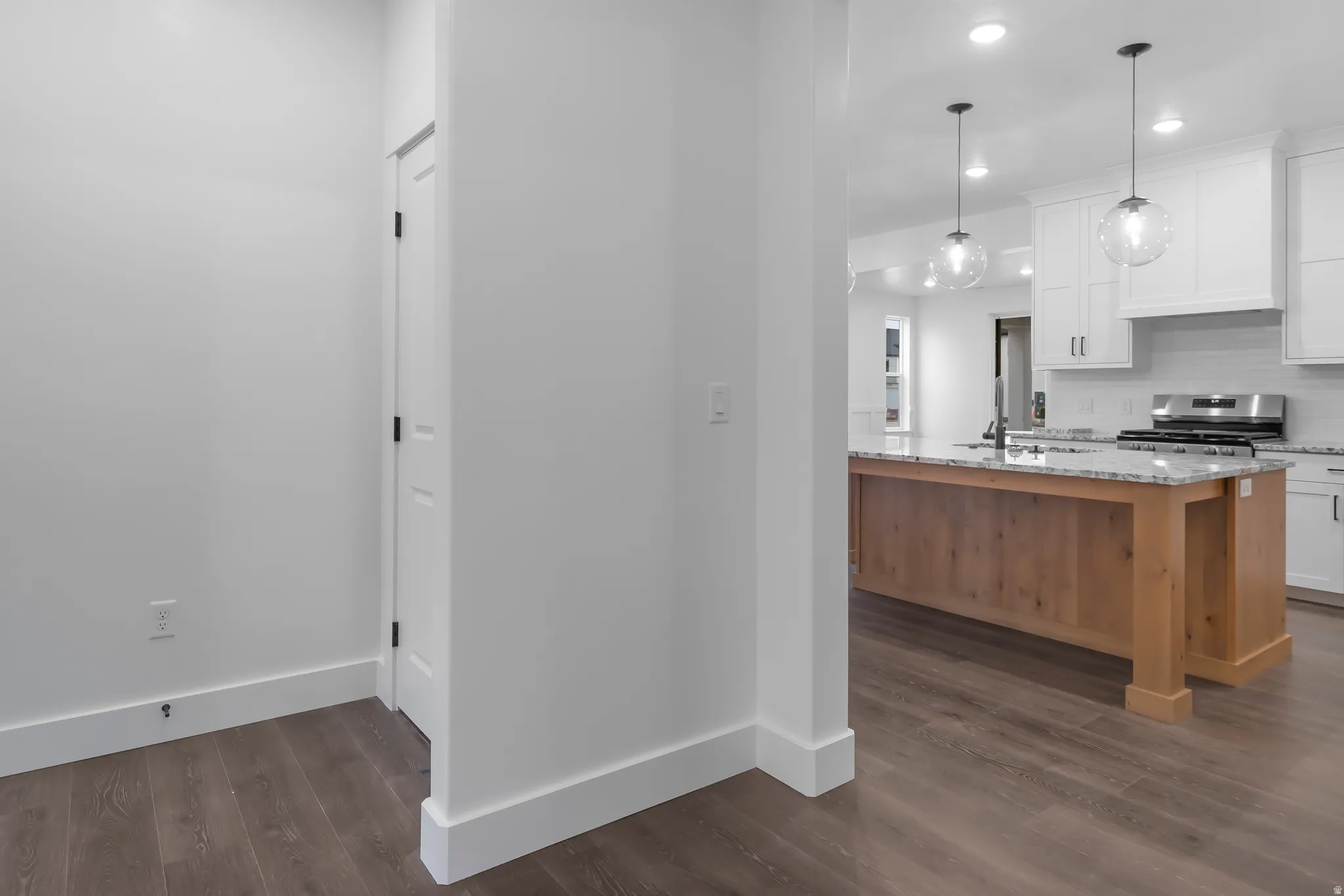 Dual tone kitchen with light stone counters, a center island with sink, decorative backsplash, stainless steel range oven, and dark wood-type flooring