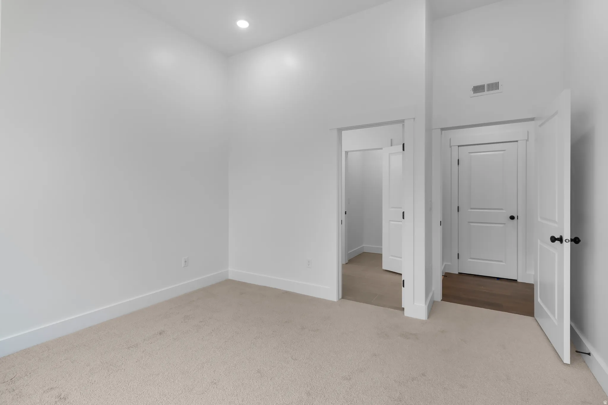 Unfurnished bedroom with light colored carpet and a high ceiling