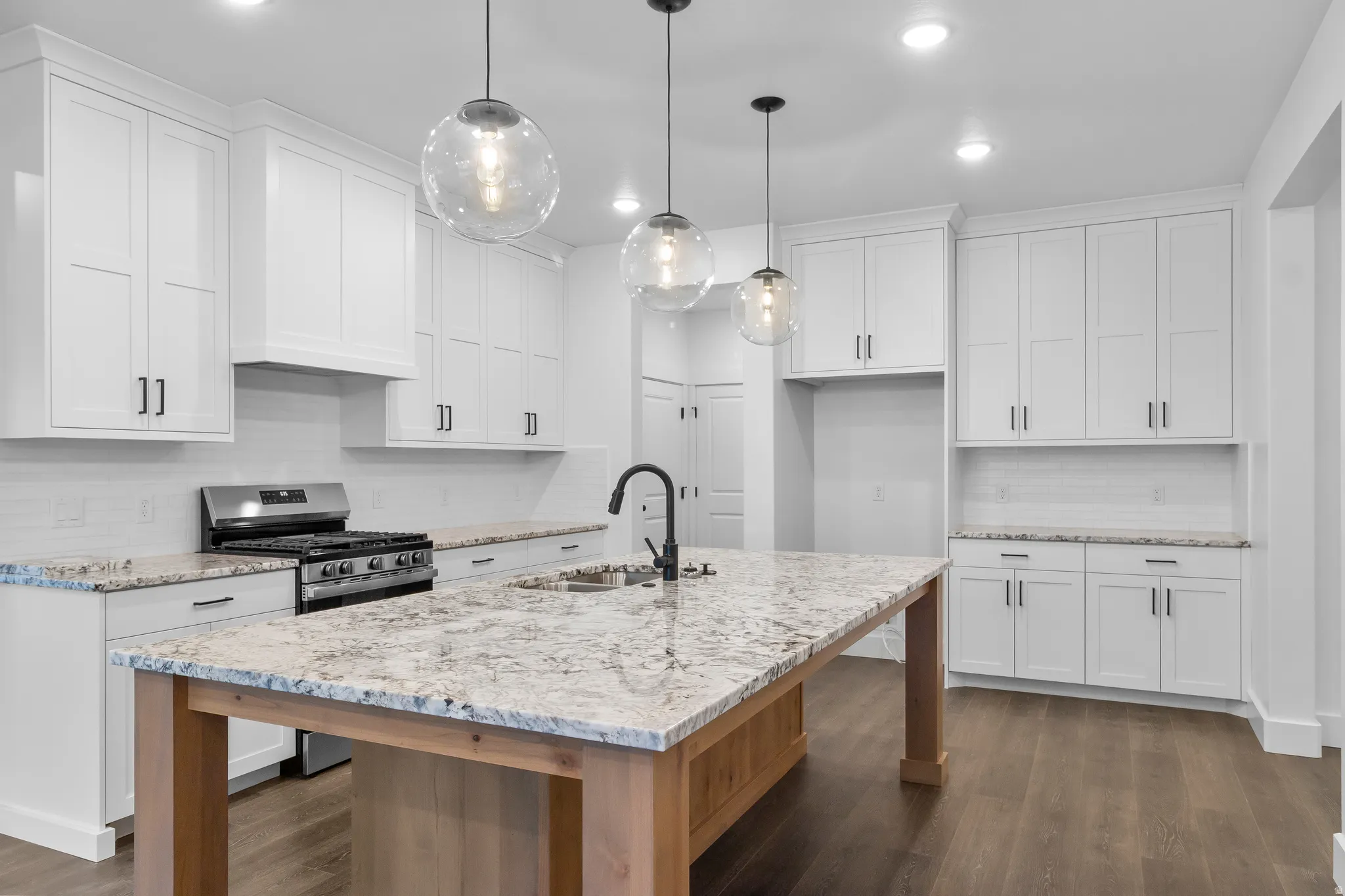 Kitchen with decorative backsplash, stainless steel gas range oven, light stone countertops, and white cabinetry