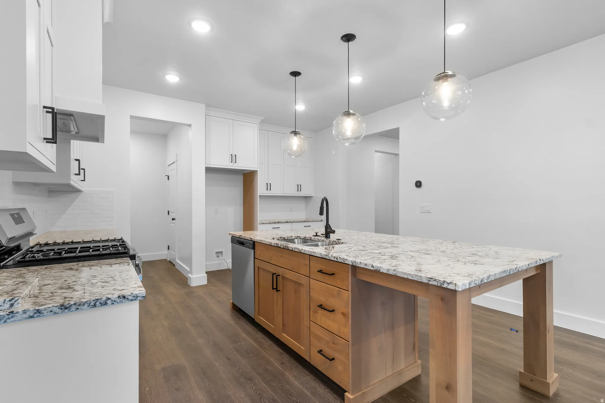 Kitchen featuring a kitchen island with sink, stainless steel appliances, light stone countertops, dark wood-style flooring, and hanging light fixtures