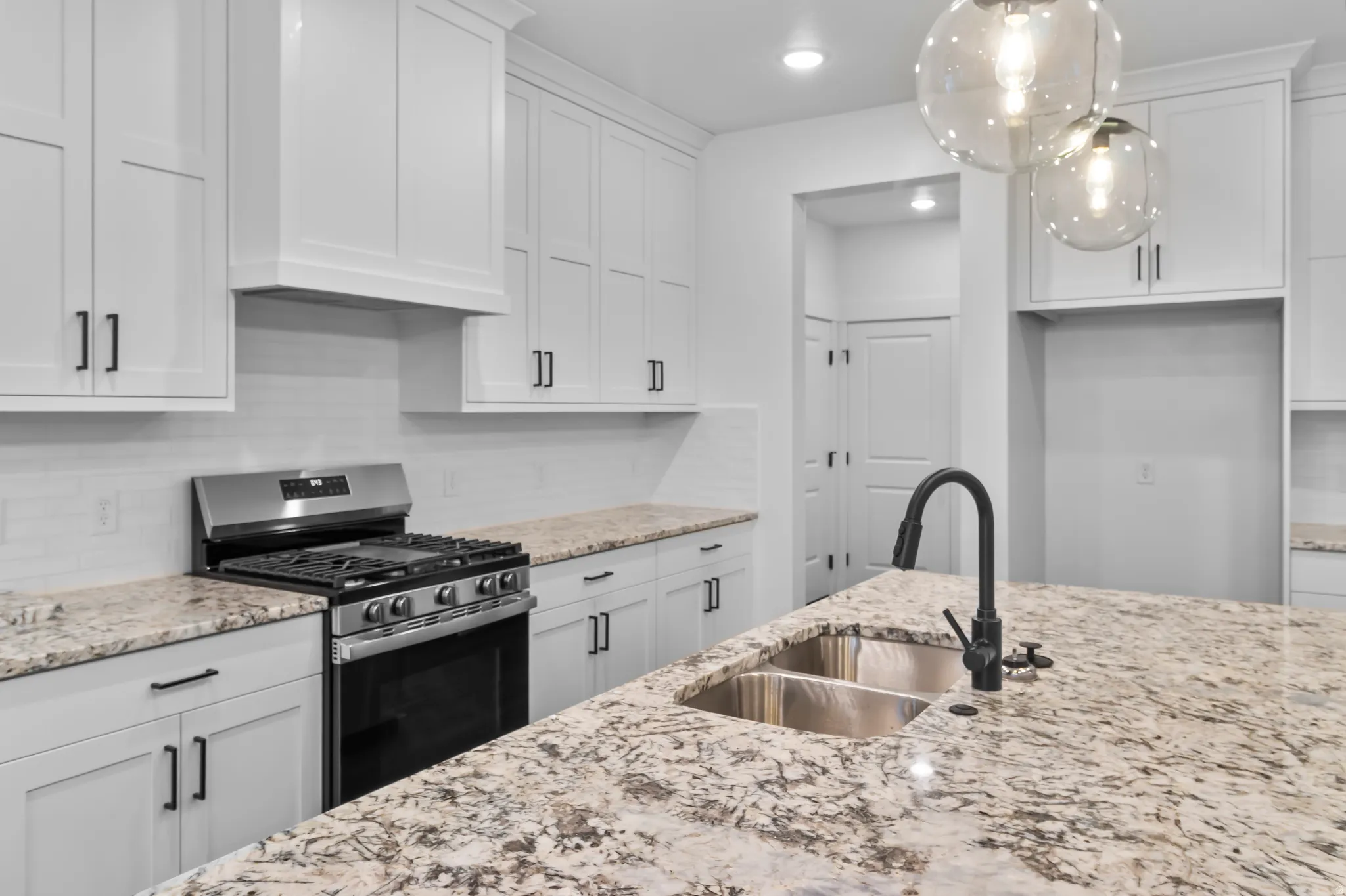 Kitchen featuring gas stove, tasteful backsplash, white cabinetry, and light stone countertops