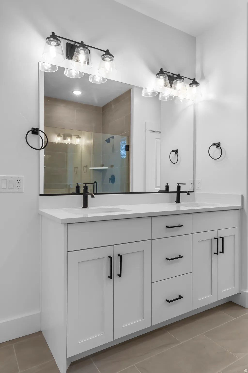 Full bathroom with double vanity, light tile patterned floors, and a shower stall