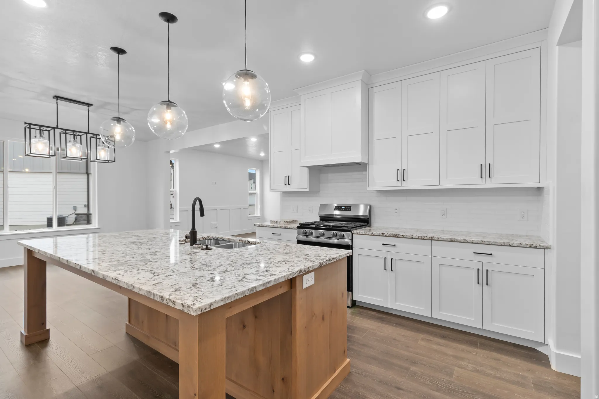 Two tone kitchen featuring light stone counters, gas stove, a center island with sink, dark wood-type flooring, and backsplash