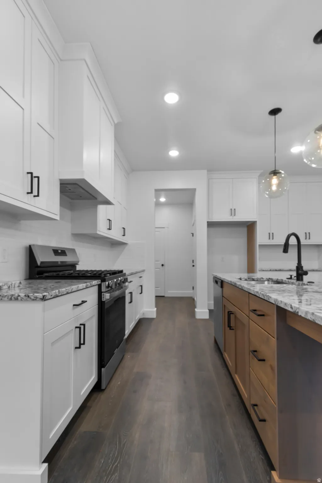 Two tone kitchen featuring stainless steel appliances, dark wood-style flooring, light stone counters, two tone color scheme, and pendant lighting