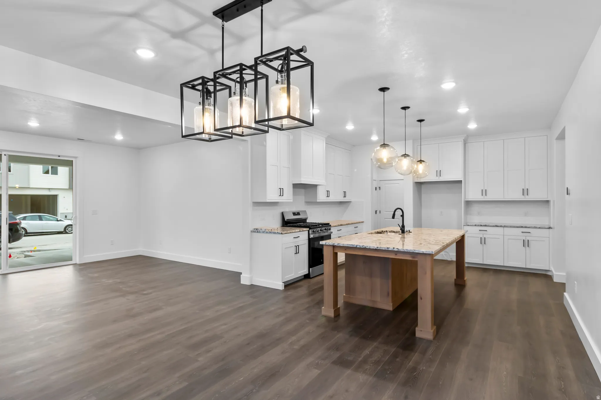 Kitchen featuring white cabinetry, gas range, light stone countertops, pendant lighting, and an island with sink