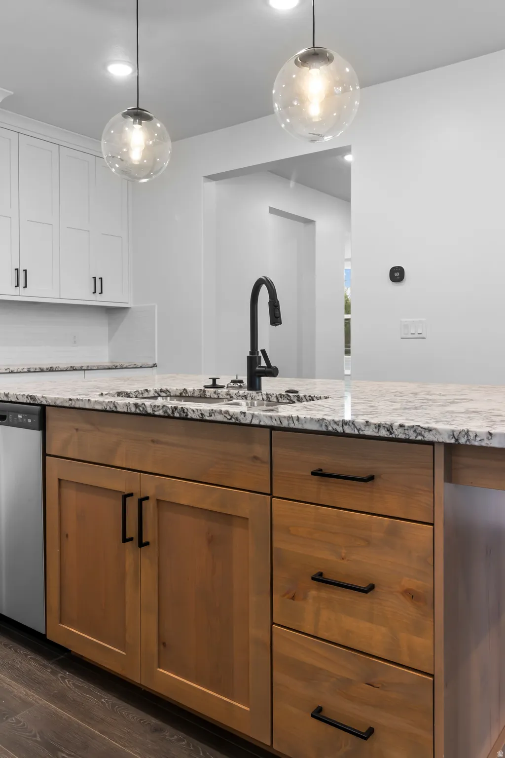 Kitchen featuring light stone counters, stainless steel dishwasher, pendant lighting, and wood finish cabinetry
