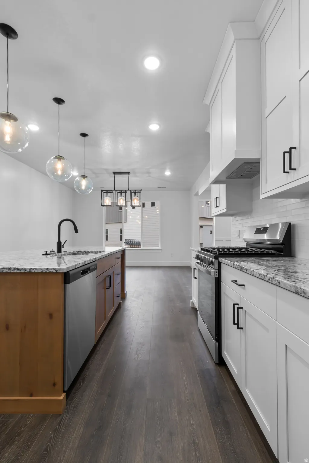 Two tone kitchen featuring stainless steel appliances, light stone countertops, dark wood-style floors, decorative light fixtures, and two tone cabinets