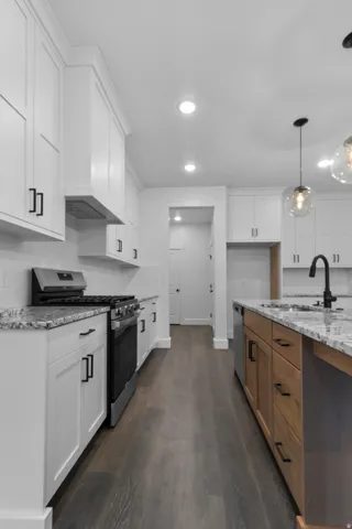 Two tone kitchen featuring stainless steel appliances, dark wood-style flooring, light stone counters, two tone color scheme, and pendant lighting