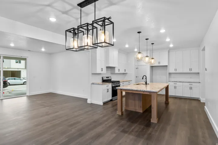 Kitchen featuring white cabinetry, gas range, light stone countertops, pendant lighting, and an island with sink