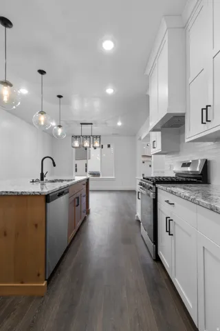 Two tone kitchen featuring stainless steel appliances, light stone countertops, dark wood-style floors, decorative light fixtures, and two tone cabinets
