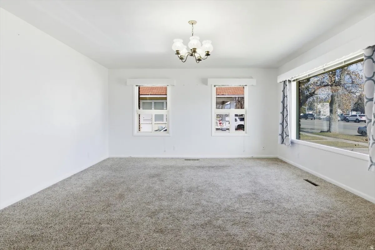 Spare room featuring carpet flooring, suspended lighting, and healthy amount of natural light