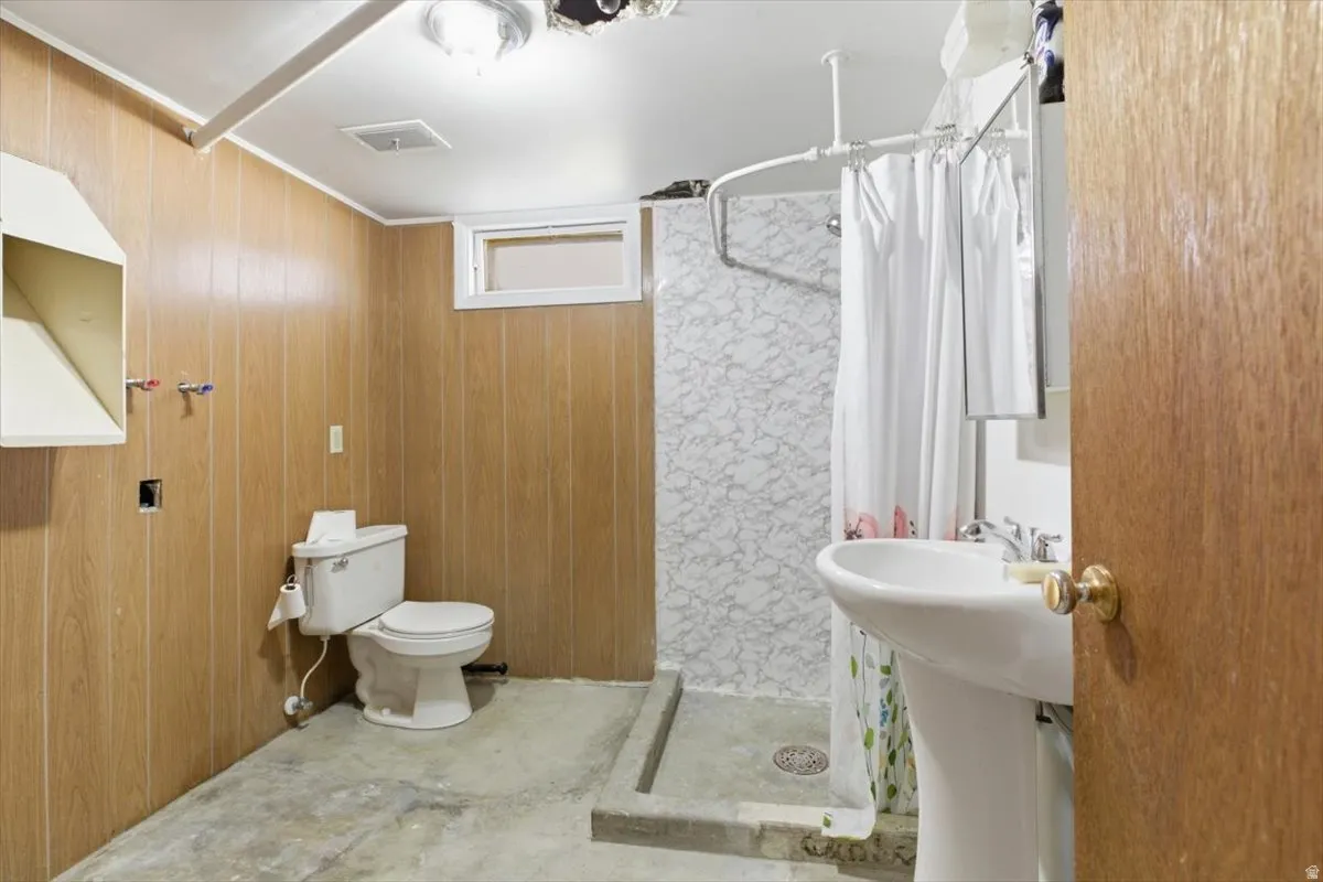 Bathroom with a shower stall, wooden walls, and concrete floors