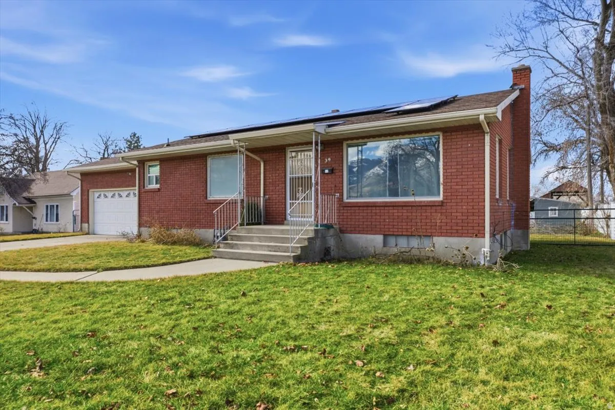 View of front of property with solar panels, a chimney, brick siding, and an attached garage
