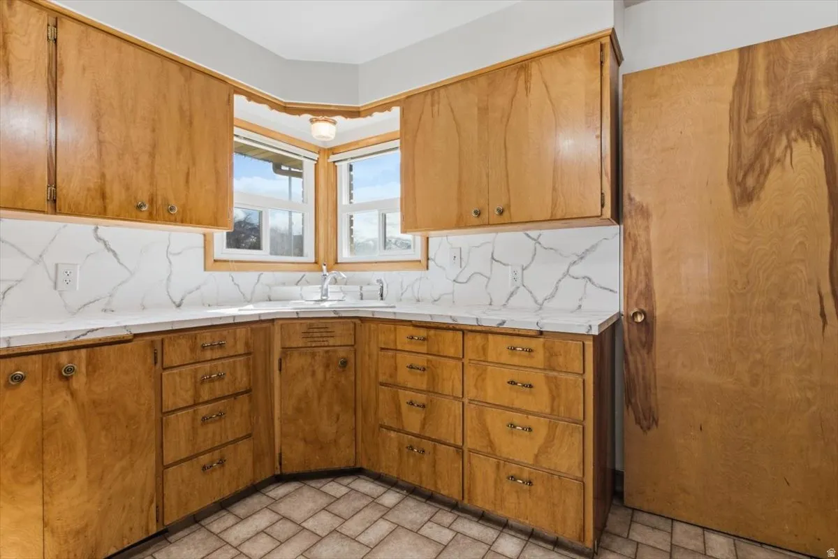 Kitchen featuring light countertops, wood finish cabinetry, tasteful backsplash, and brick patterned flooring