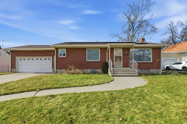 Single story home with brick siding, an attached garage, roof mounted solar panels, and driveway