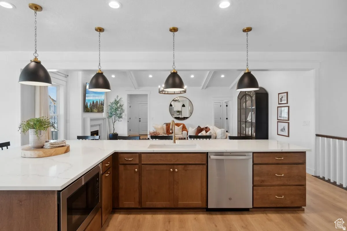 Kitchen with light stone counters, stainless steel appliances, beamed ceiling, light wood-style floors, and open floor plan