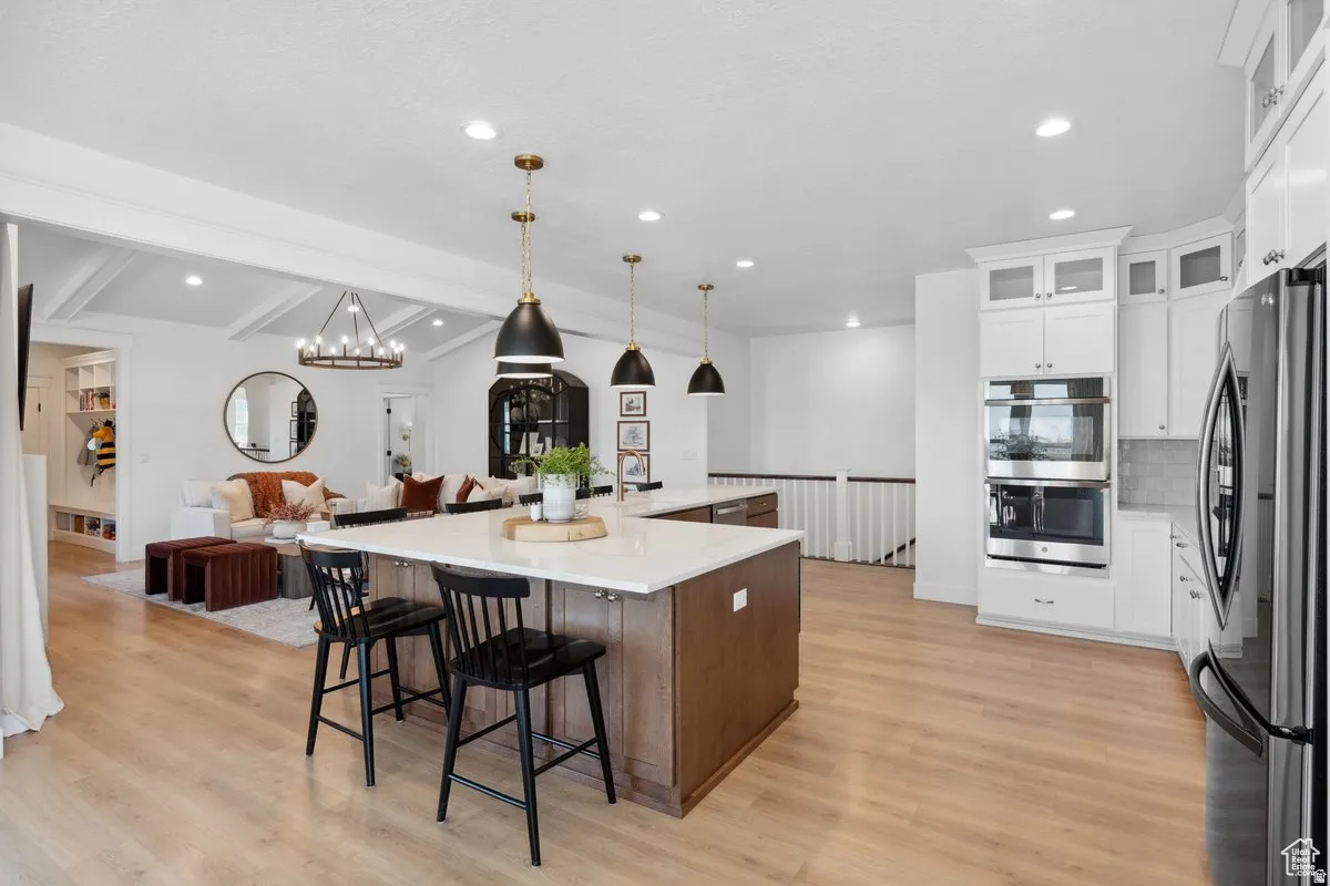 Dual tone kitchen featuring stainless steel appliances, open floor plan, a spacious island, a breakfast bar, and light stone counters