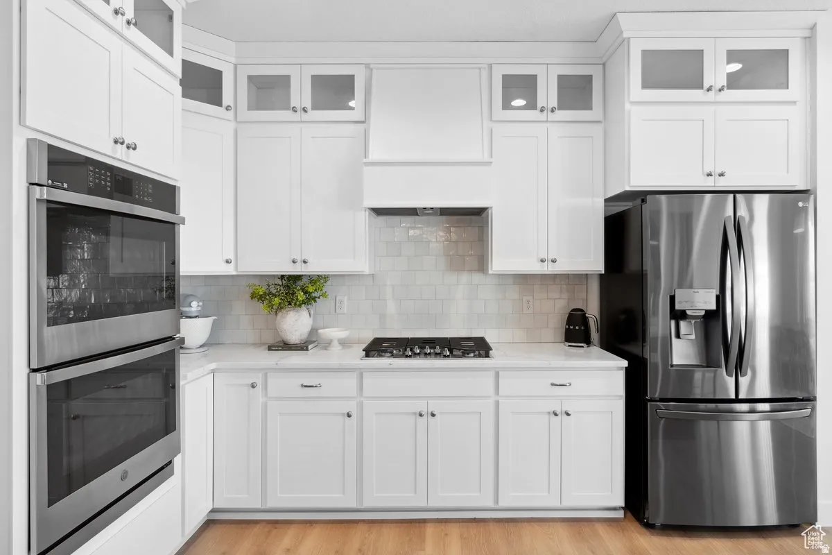 Kitchen with stainless steel appliances, white cabinets, tasteful backsplash, light stone counters, and light wood-style flooring