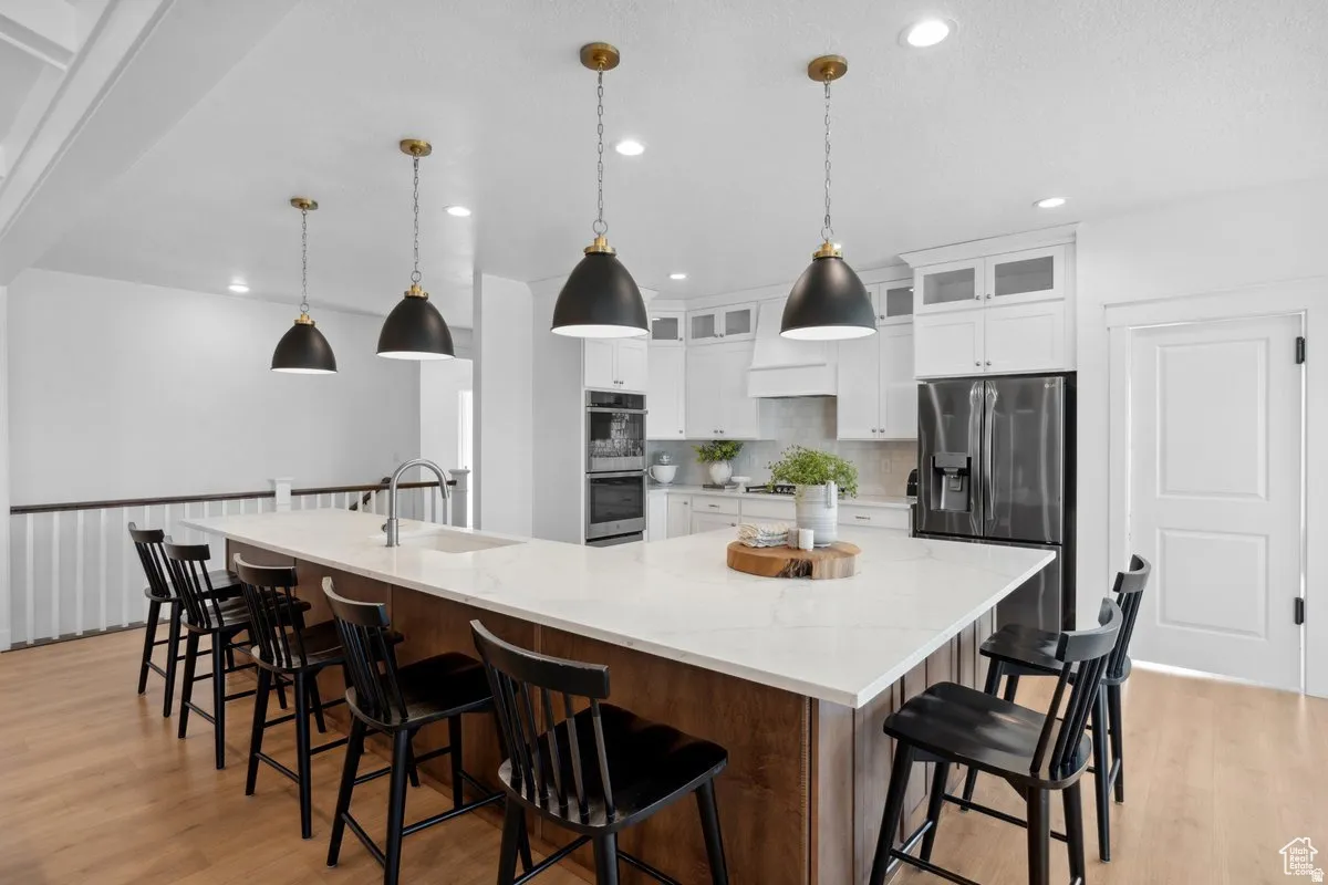 Two tone kitchen with a breakfast bar, light wood-style flooring, glass insert cabinets, light stone counters, and a large island with sink