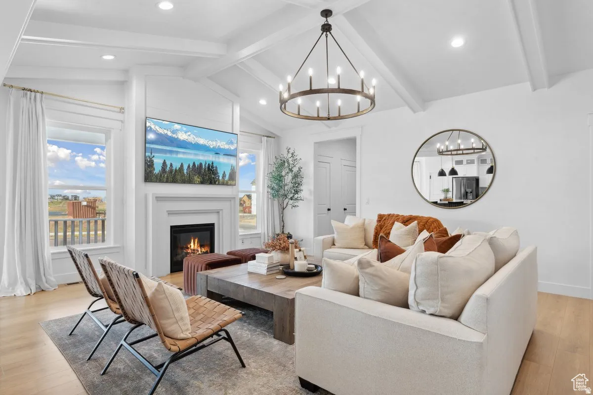 Living room with light wood finished floors, suspended lighting, beam ceiling, and a glass covered fireplace