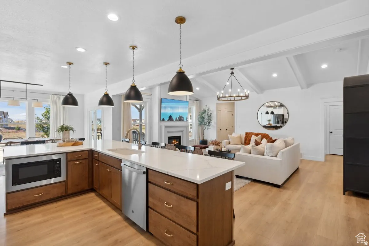 Kitchen featuring open floor plan, a warm lit fireplace, light wood finished floors, stainless steel appliances, and suspended lighting