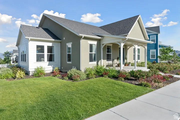 View of side of home with a yard, covered porch, a shingled roof, and stucco siding