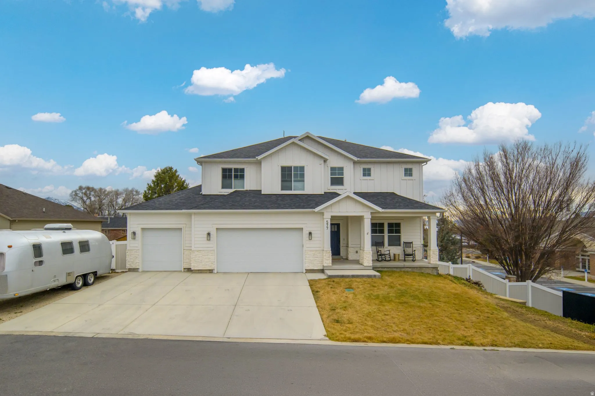 Traditional home with a porch, stone siding, board and batten siding, driveway, and an attached garage