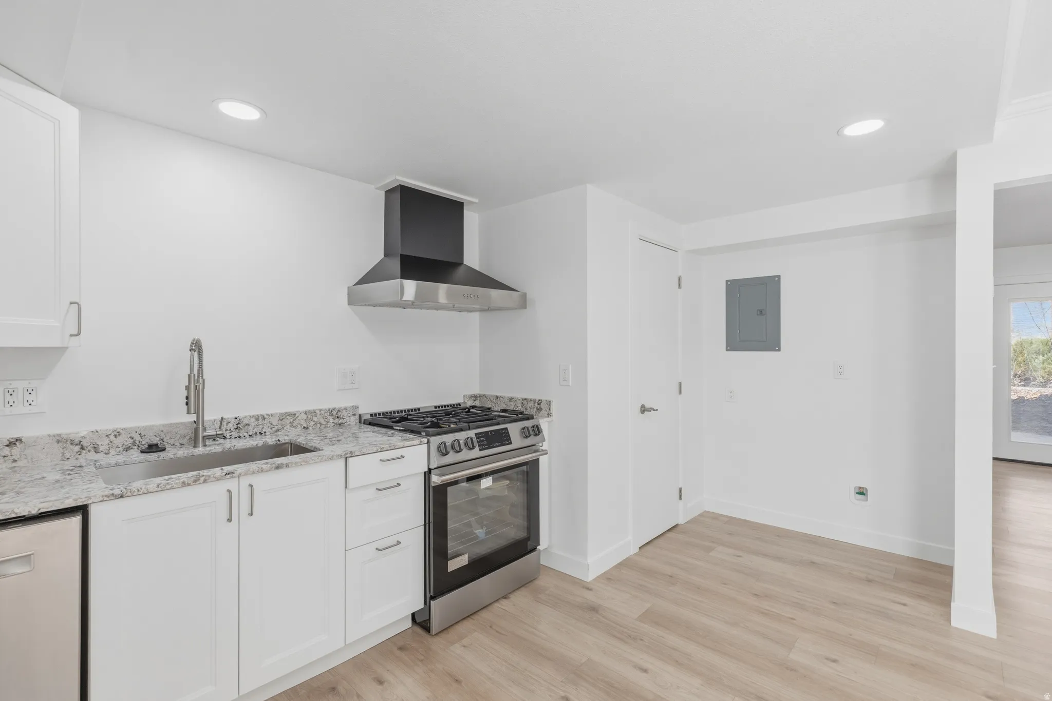 Kitchen featuring stainless steel gas range, light wood-style flooring, light stone countertops, white cabinets, and recessed lighting