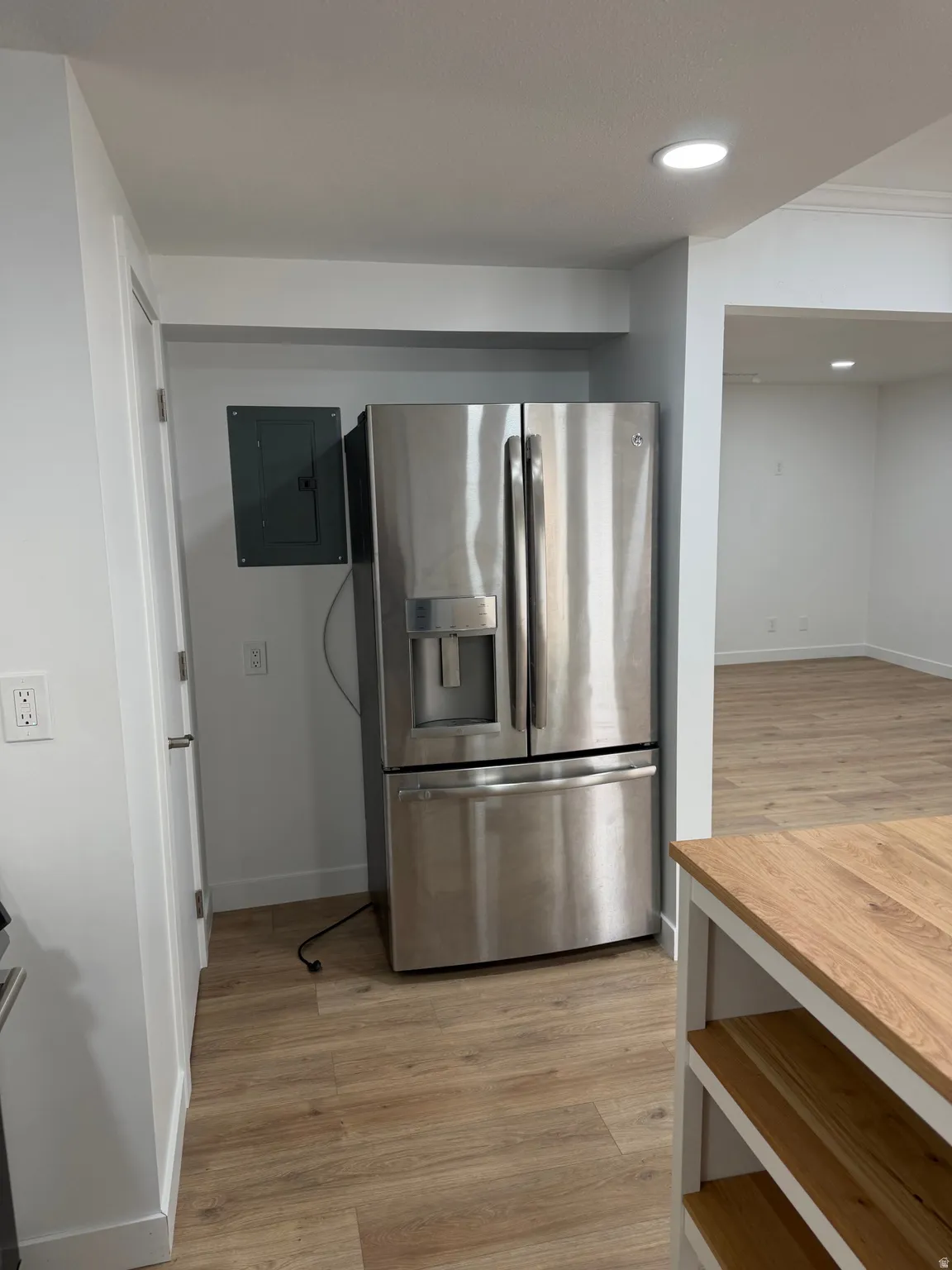 Stainless steel French-door refrigerator, wood-finish flooring, recessed lighting, and a kitchen island with a natural wood countertop