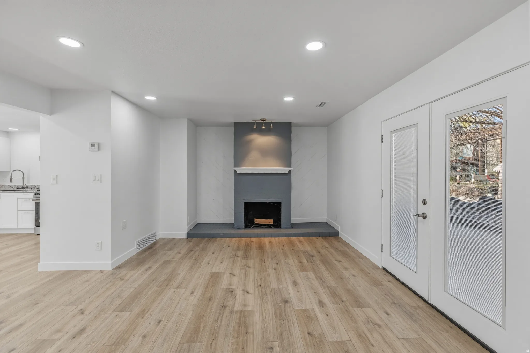 Unfurnished living room featuring recessed lighting, light wood-style flooring, a fireplace with raised hearth, and french doors