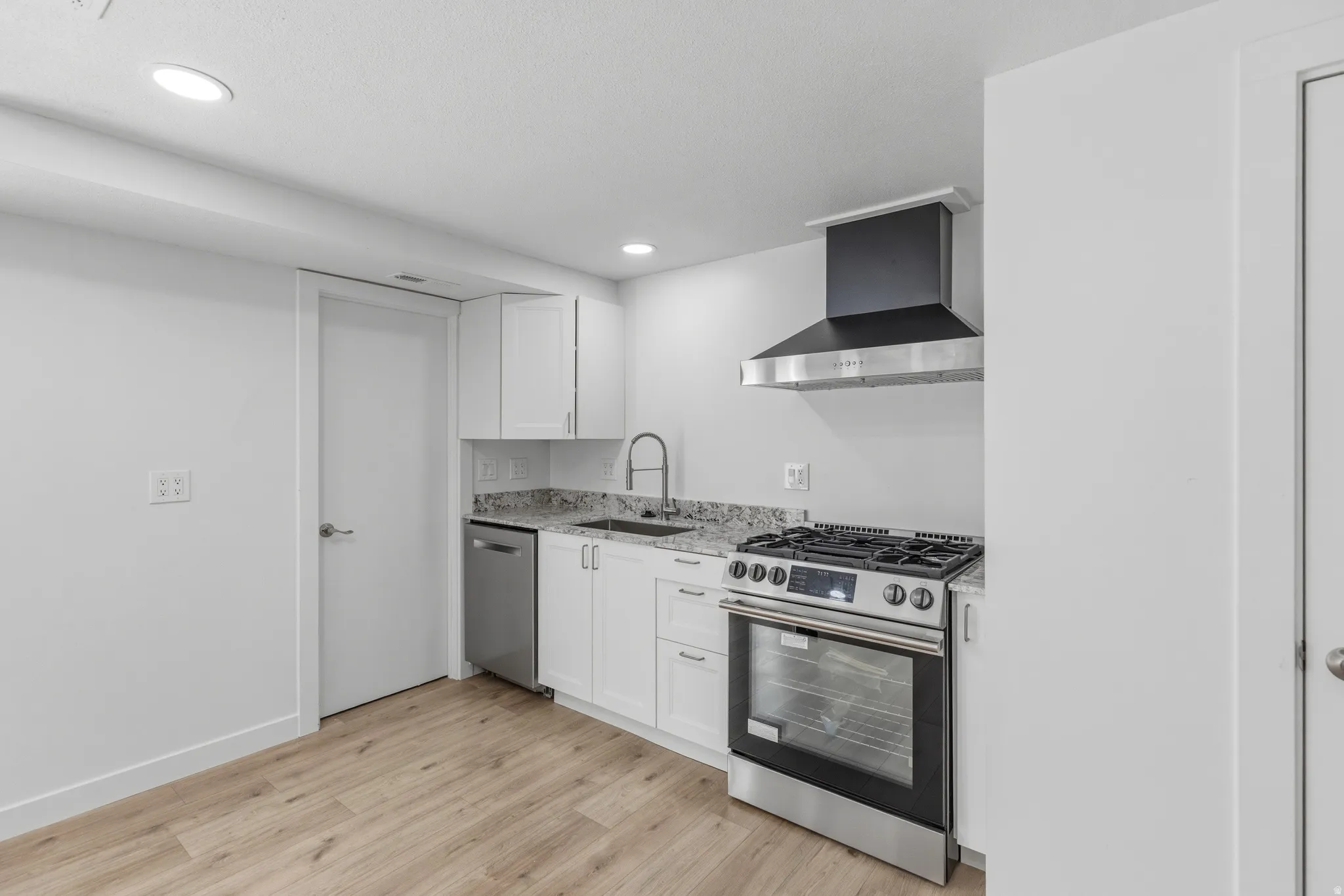 Kitchen with stainless steel appliances, white cabinetry, light stone countertops, light wood finished floors, and recessed lighting