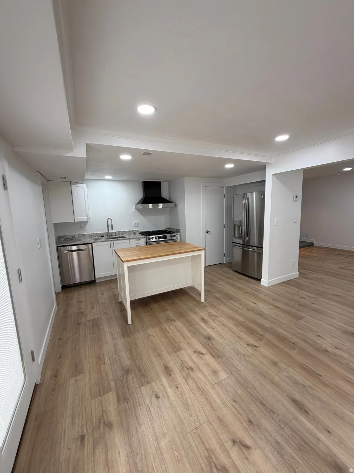Open-concept kitchen featuring an island with a wood-finish countertop, stainless steel appliances, white cabinetry, and recessed lighting